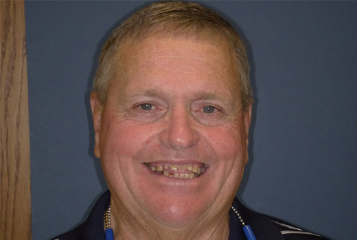 Smiling man in professional attire against blue background, dental practice portrait.