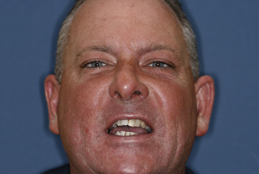 Middle-aged man smiling at camera against blue background, professional headshot