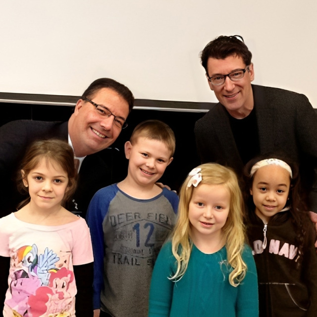 Two dental professionals posing with four smiling children in front of a neutral background.