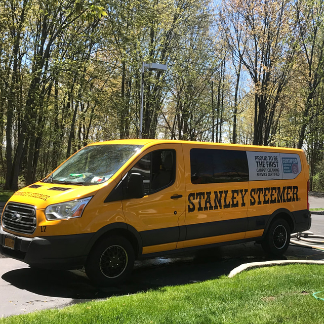 Yellow Stanley Steemer van parked on tree-lined street for carpet cleaning service.