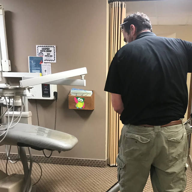Man standing in dental examination room with chair and equipment visible.