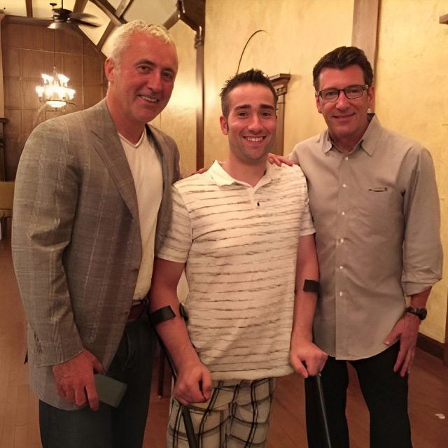 Three men smiling together indoors at what appears to be a social or professional gathering.