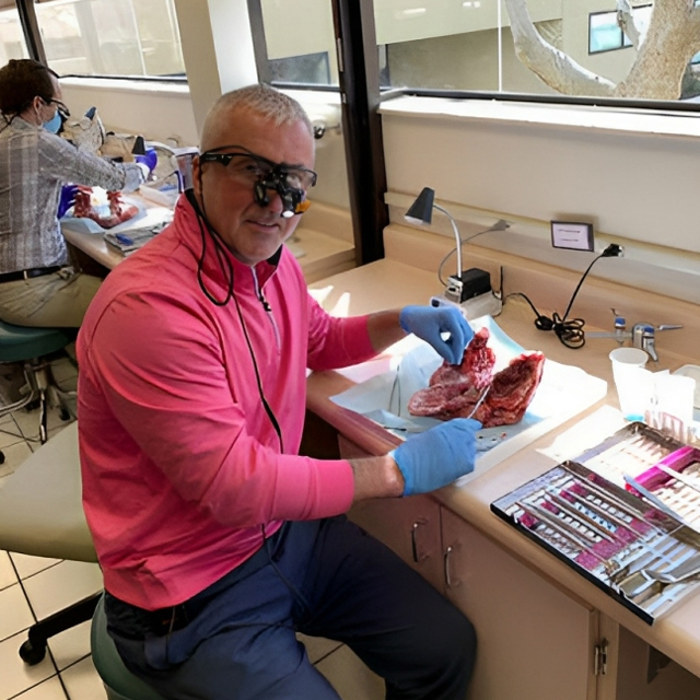 Man in pink shirt examining dental specimen with magnifying glasses in clinical laboratory setting.