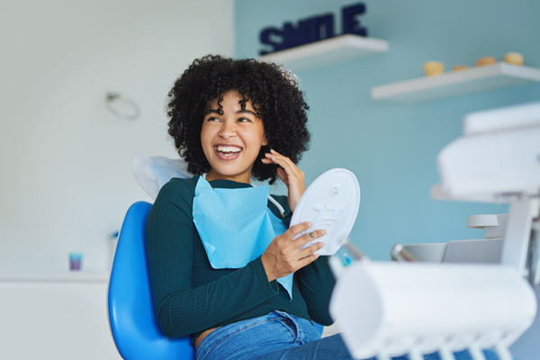Happy patient holding mirror in modern dental office chair during consultation.