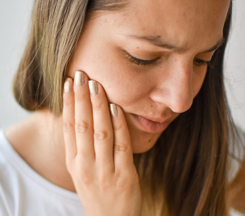 Woman experiencing tooth pain, holding jaw with hand against white background.