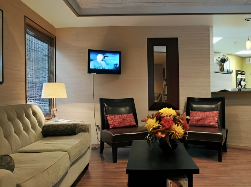 Modern dental office waiting room with cream sofa, black chairs, and flat-screen TV.