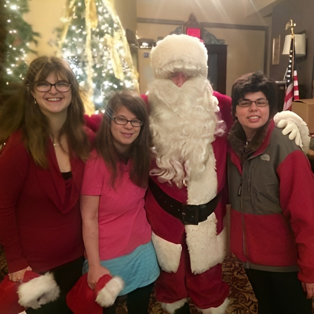 Four young people posing with Santa Claus at a festive holiday event indoors.