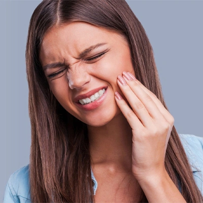 Woman touching her cheek in pain, grimacing with dental discomfort against neutral background.